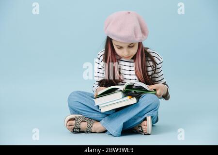 Petite fille à la mode en béret français assis à pattes croisées, livre de lecture Banque D'Images