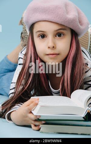 Petite fille pensive dans le béret français couché sur le sol, livre de lecture Banque D'Images