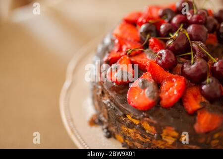 Gâteau au chocolat maison traditionnel dessert sucré avec glaçage brun, cerises, framboise, cassis sur fond de bois vintage. Photo de nourriture sombre Banque D'Images