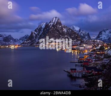 Une photo aérienne hypnotique d'un village de pêcheurs illuminé avec des maisons de rorbu sous le ciel violet du soir à Reine, île Lofoten, Norvège Banque D'Images