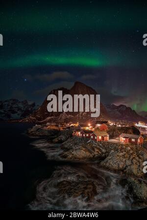 Un cliché vertical d'aurora borealis sur un village de pêche éclairé avec des maisons de rorbu à Homnoya, île Lofoten, Norvège Banque D'Images