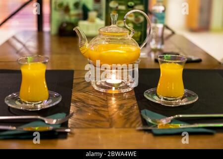 une théière en verre avec de délicieux busthorn de vitamine de mer et de thé de miel se tient sur un support avec une bougie chauffante et à côté de lui sont des tasses en verre. gros plan Banque D'Images