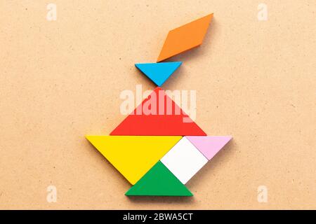 Puzzle de couleur en forme de tangram dans un chandelier sur un bacille de bois Banque D'Images