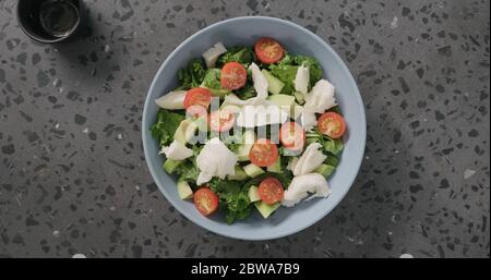 Salade vue de dessus avec tomates, avocat, mozzarella et feuilles de kale dans un bol en céramique bleu sur fond de béton Banque D'Images