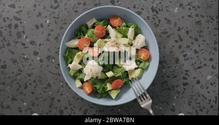 Salade vue de dessus avec tomates, avocat, mozzarella et feuilles de kale dans un bol en céramique bleu sur fond de béton Banque D'Images