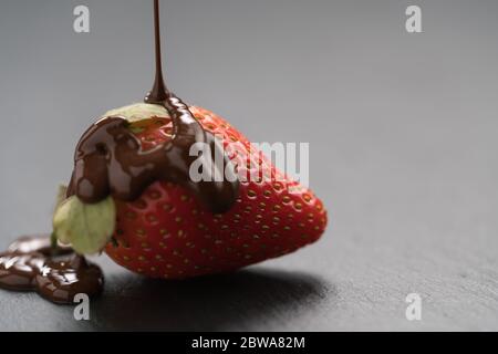 Verser le chocolat sur la fraise mûre sur fond d'ardoise Banque D'Images