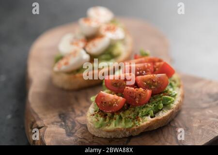 Bruschettas avec avocat, tomate et mozzarella sur panneau de bois sur bacille en béton Banque D'Images