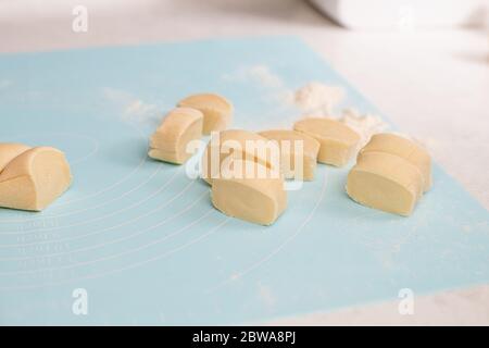 Préparation de biscuits, boulettes, biscuits, plats de pâtisserie avec tapis bleu roulant de silicone, gros plan coupé directement par des morceaux de couteau de pâte crue Banque D'Images