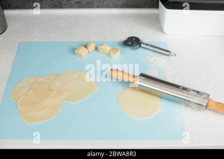 Processus de laminage et de découpe de pâte brute avec tapis de pâtisserie, couteau, broche sur table, cuisson à la table de cuisson de près Banque D'Images