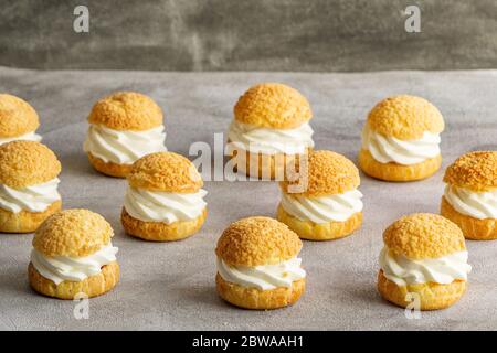 Biscuits de pâte Chou FilleCous biscuits de pâte fourrés de crème fouettée sur fond gris. Concept: Boulangerie, dessert français. d avec crème fouettée sur fond gris. Concept: Boulangerie, dessert français. . Photo de haute qualité Banque D'Images