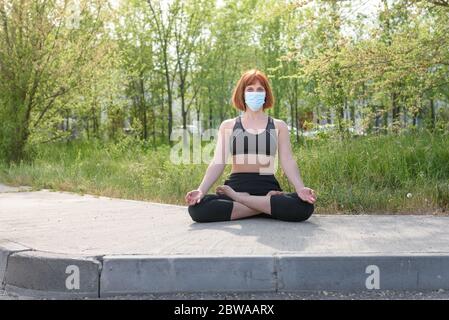 Fille en position lotus avec masque sirurgical dans fond de nature. Concept de coronavirus Banque D'Images