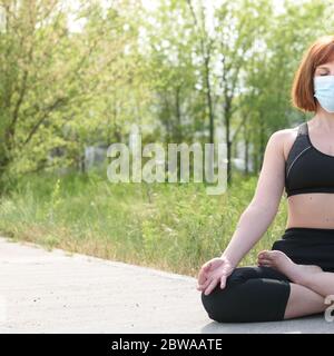 Fille en position lotus avec masque sirurgical dans fond de nature. Concept de coronavirus Banque D'Images