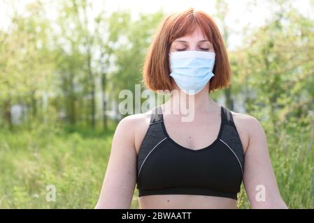 Fille en position lotus avec masque sirurgical dans fond de nature. Concept de coronavirus Banque D'Images