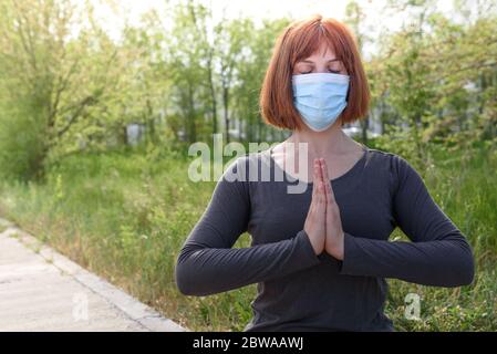 Fille en position lotus avec masque sirurgical dans fond de nature. Concept de coronavirus Banque D'Images