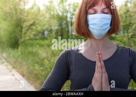 Fille en position lotus avec masque sirurgical dans fond de nature. Concept de coronavirus Banque D'Images