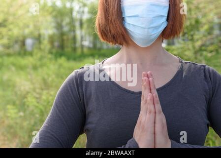 Fille en position lotus avec masque sirurgical dans fond de nature. Concept de coronavirus Banque D'Images