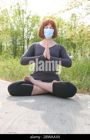 Fille en position lotus avec masque sirurgical dans fond de nature. Concept de coronavirus Banque D'Images