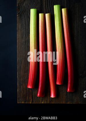 Tiges de rhubarbe fraîches sur planche en bois prêtes à hacher, fond noir, vue de dessus Banque D'Images