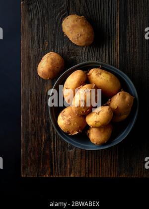 Bol de pommes de terre neuves sur bois prêt à cuire, fond noir, vue de dessus Banque D'Images