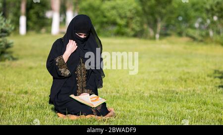 La femme islamique effectue la prière du matin, assise sur l'herbe verte dans le parc. Banque D'Images
