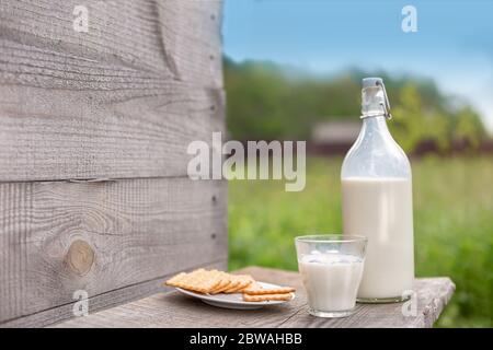 Une bouteille de lait frais, un verre et une petite assiette avec des craquelins sur une table en bois, près d'un mur en bois donnant sur un champ vert et un ciel bleu. Station santé Copy Banque D'Images