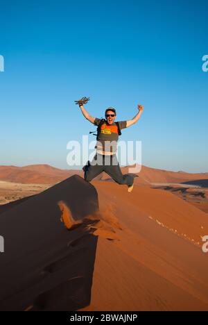 Un jeune homme heureux sautant au sommet d'une dune de sable dans le désert du Namib près de Sousssusvlei en Namibie, en Afrique Banque D'Images