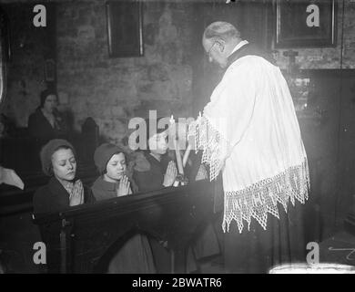 La cérémonie annuelle de la Bénédiction de St Blaise ( Bénédiction des gorges de la congrégation ) à l'église de St Etheldreda , Ely place , Londres . Père Baines exécutant la cérémonie . 2 février 1936 Banque D'Images