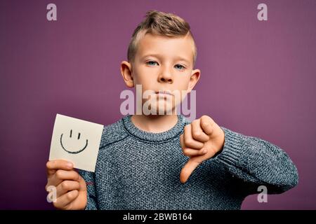 Jeune petit casien montrant le visage smiley sur une note de papier comme un message heureux avec le visage en colère, signe négatif montrant le désairoi avec les pouces vers le bas, rejec Banque D'Images