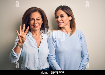 Âge moyen beau couple de sœurs debout sur un fond blanc isolé montrant et pointant vers le haut avec les doigts numéro quatre tout en souriant confiden Banque D'Images