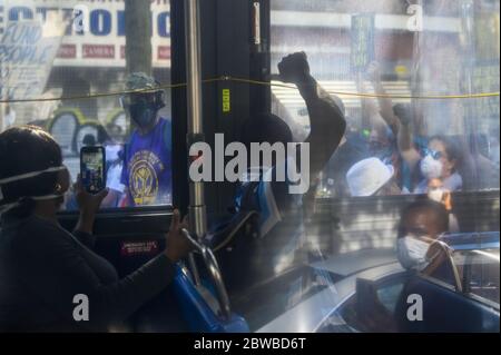 Un homme dans un autobus de ville lève son poing en solidarité avec les personnes de Black Lives Matter manifestants lors d'un affrontement avec les officiers de police de NYPD alors que les manifestations dans tout le pays se poursuivent à la suite de la mort de George Floyd aux mains de la police de Minneapolis dans les jours de la pandémie du coronavirus New York le samedi 30 mai 2020. L'ancien policier de Minneapolis Derek Chauvin a été arrêté vendredi jours après que la vidéo a circulé de lui tenant son genou au cou de George Floyd pendant plus de huit minutes avant la mort de Floyd. Les quatre agents impliqués dans l'incident ont également été congédiés du polic de Minneapolis Banque D'Images