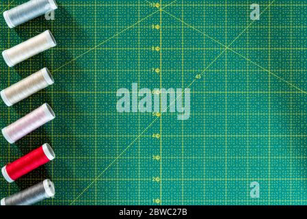 Coupage à plat. Vue de dessus des fils colorés sur le tapis de coupe vert. Industrie de la couture, artisanat et passe-temps de couture Banque D'Images