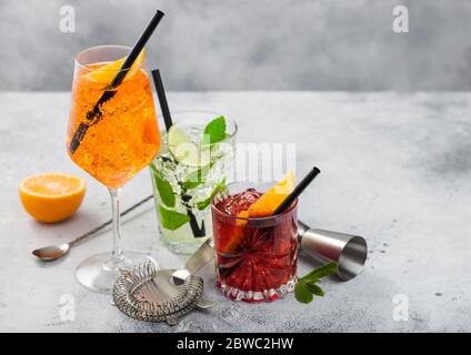 Verres de cocktails Spritz, mojito et negroni avec glaçons et tranches de citron vert et orange avec feuille de menthe et paille noire sur fond de table clair avec Banque D'Images