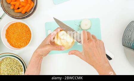 Recette de soupe de lentilles. Chef épluchant l'oignon blanc, vue rapprochée du dessus, fond blanc de la table de cuisine Banque D'Images