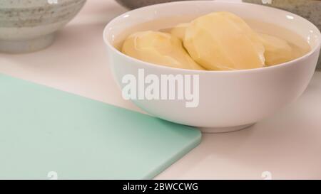 Pommes de terre pelées dans un bol, en gros plan sur une table de cuisine blanche Banque D'Images