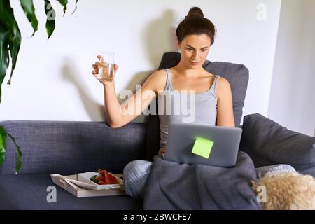 la femme travaille à domicile et boit de l'eau pendant une pandémie au ralenti Banque D'Images