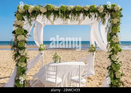 Cérémonie de mariage romantique luxueuse sur l'océan, la plage. L'arche en bois est décorée de fleurs fraîches et de tulles blanches. Banque D'Images