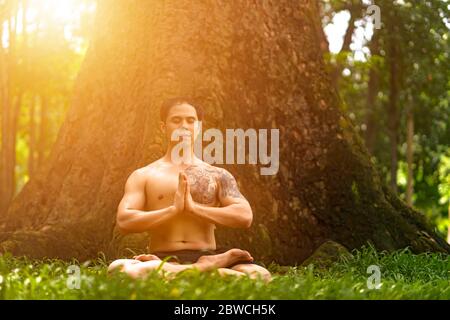 Un jeune homme asiatique se fait suer et faire des exercices de yoga dans le parc. Yoga et concept zen. Banque D'Images