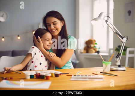 Une maman heureuse embrasse une fille qui s'assoit à la table de la chambre. Banque D'Images