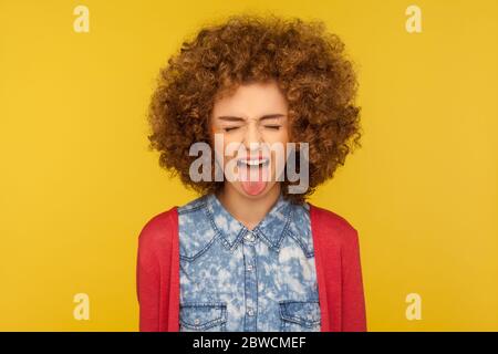 Portrait de femme drôle délirante avec cheveux bouclés dans une tenue décontractée montrant la langue et fermé ses yeux déplaisantés, se comportant indiscipliné rire. Banque D'Images