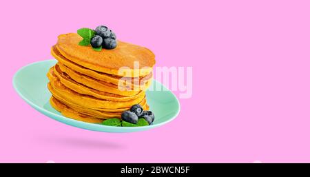 Tas de crêpes de citrouille avec des bleuets et de la menthe sur une assiette turquoise isolée sur fond rose. Copier l'espace Banque D'Images