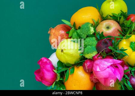 Composition de fruits, légumes et fleurs sur fond vert avec espace de copie. Grenade, orange, poire, pamplemousse, pomme, brocoli, paprika, Banque D'Images