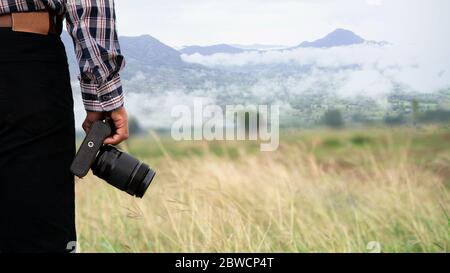 Gros plan d'un photographe tenant l'appareil photo debout sur un fond vert naturel Banque D'Images