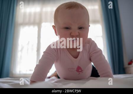 Adorable petite fille debout sur le lit faire des visages drôles, visage en colère, pleurant le matin Banque D'Images