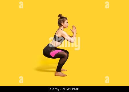 Femme sportive avec un petit pain dans les vêtements de sport serré faisant de la squat, sport du corps inférieur exercice, maintien de l'équilibre, échauffement et muscles d'entraînement. Pleine longueur Banque D'Images