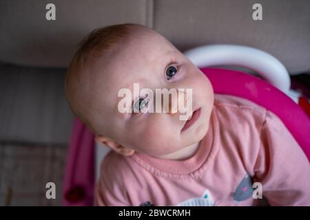 Vue en grand angle de la mignonne blonde bébé fille regardant jusqu'à l'appareil photo dans le marcheur de bébé Banque D'Images
