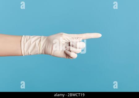 Vue latérale du profil gros plan de la main humaine avec des gants chirurgicaux blancs montrant ou pointant vers un sujet avec le doigt. Vue en studio, à l'intérieur, isolée sur une bande bleue Banque D'Images