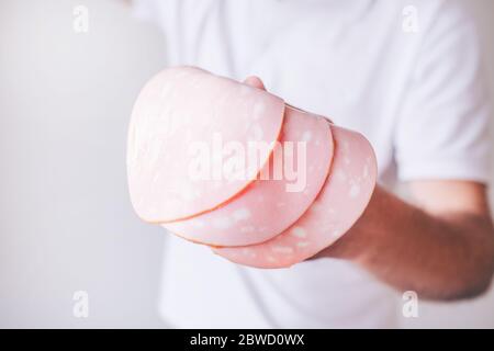 Jeune homme en chemise blanche isolée sur fond blanc. Vue en coupe de délicieux jambon en tranches à la main. Guy tient-le en main. Banque D'Images