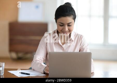 Femme d'affaires indienne positive travaillant sur un ordinateur portable, assise au bureau. Banque D'Images