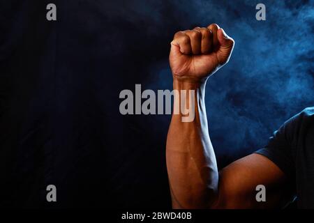 Image de studio représentant un poing afro-américain tenu en force, unité et défi avec un fond de fumée et des lumières bleues représentant la police. Banque D'Images