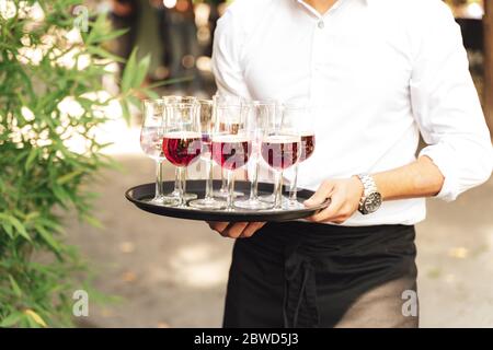 Homme portant un plateau avec plusieurs boissons colorées. Un serveur sert des boissons. Célébration, anniversaire, fête, mariage. Banque D'Images